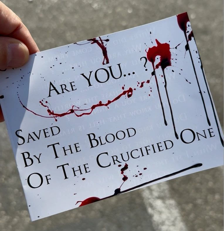 A hand holding the tract: “Are you… saved by the blood of the Crucified One?” printed over red spatter